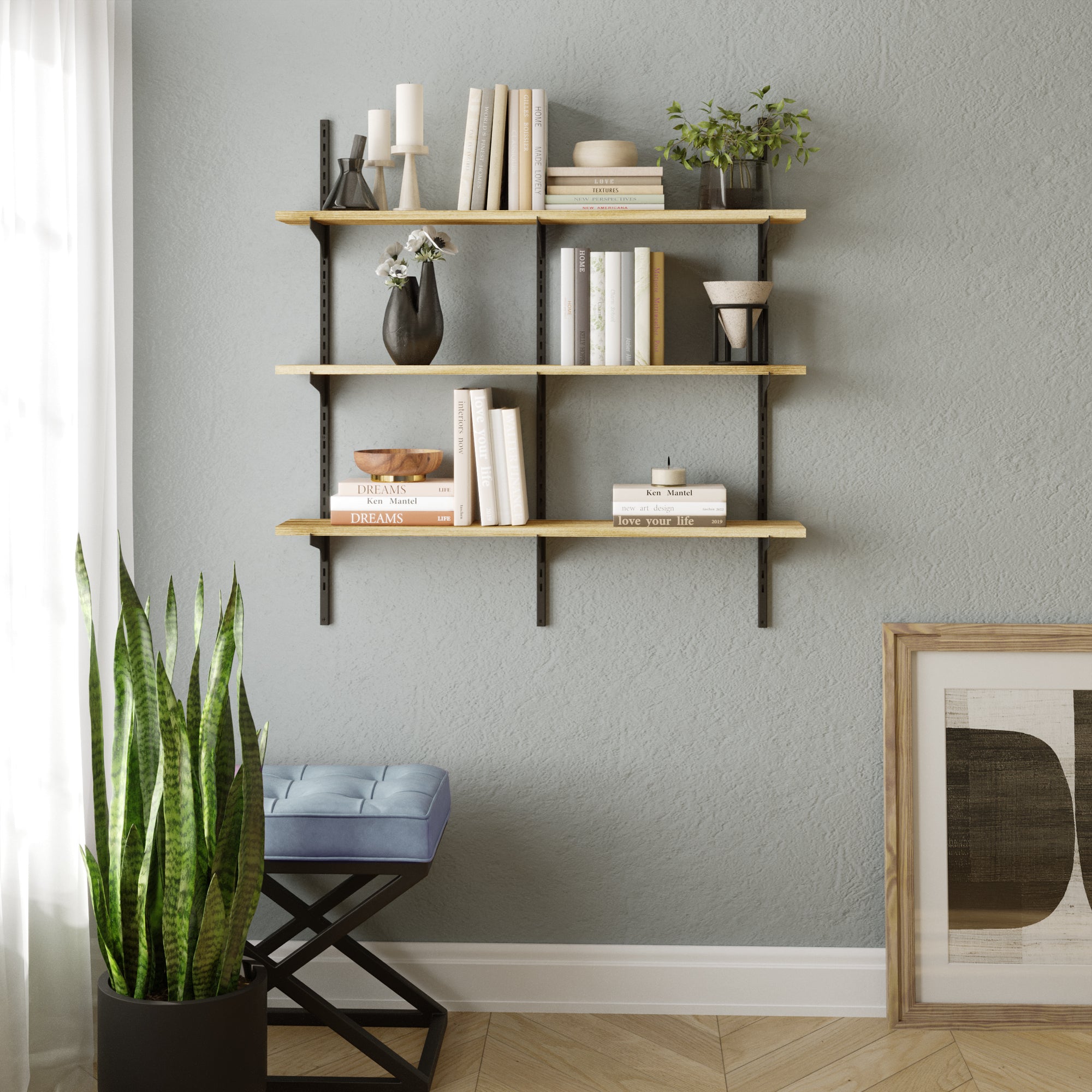 Stylish home living room setup featuring a 3-tier wall shelf for books and collectibles with light wood boards and black brackets, decorated with books, vases, and greenery above a soft blue stool.
