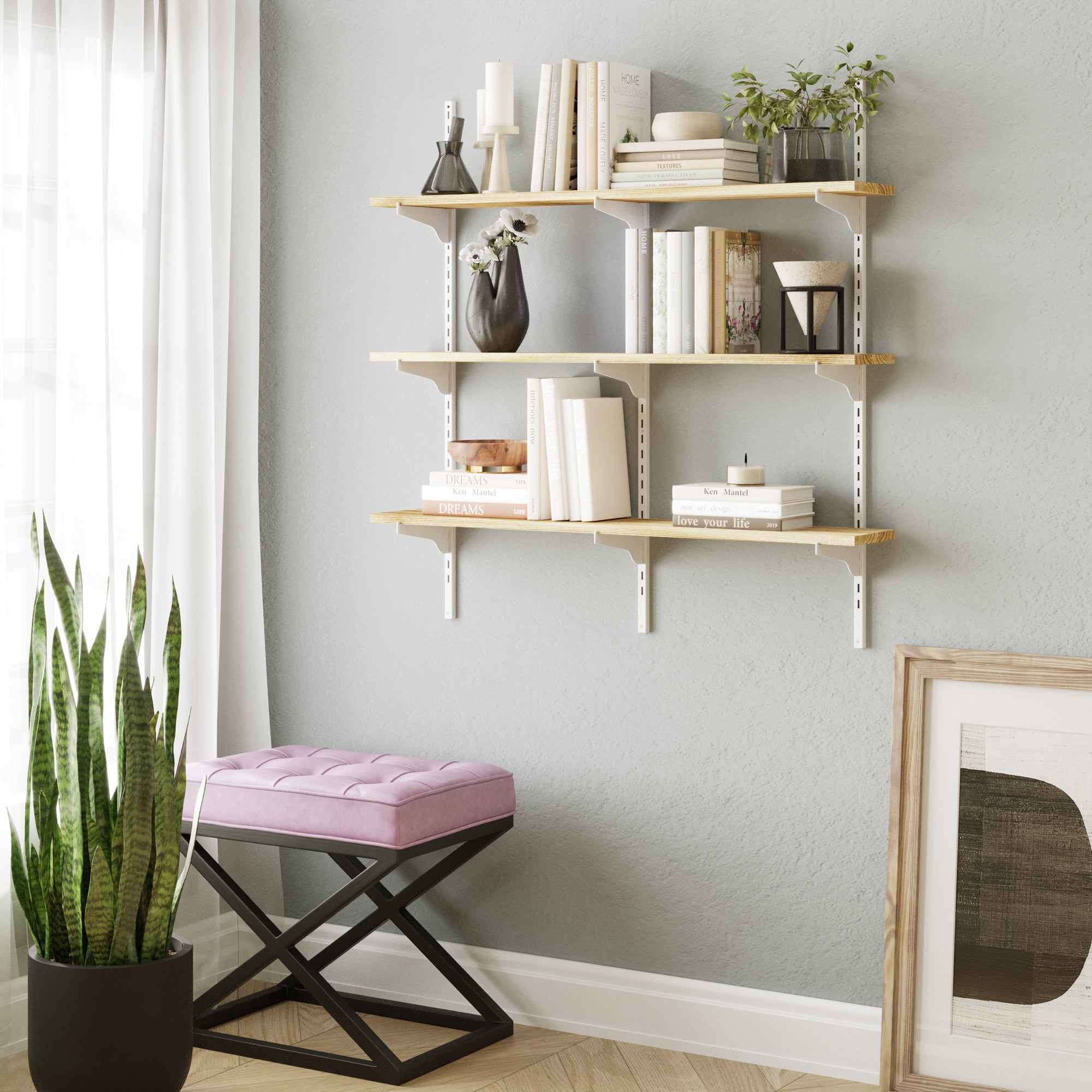 Multi tier farmhouse shelving unit with books and decor items against a light gray wall, with a pink cushioned stool and plant in the foreground.