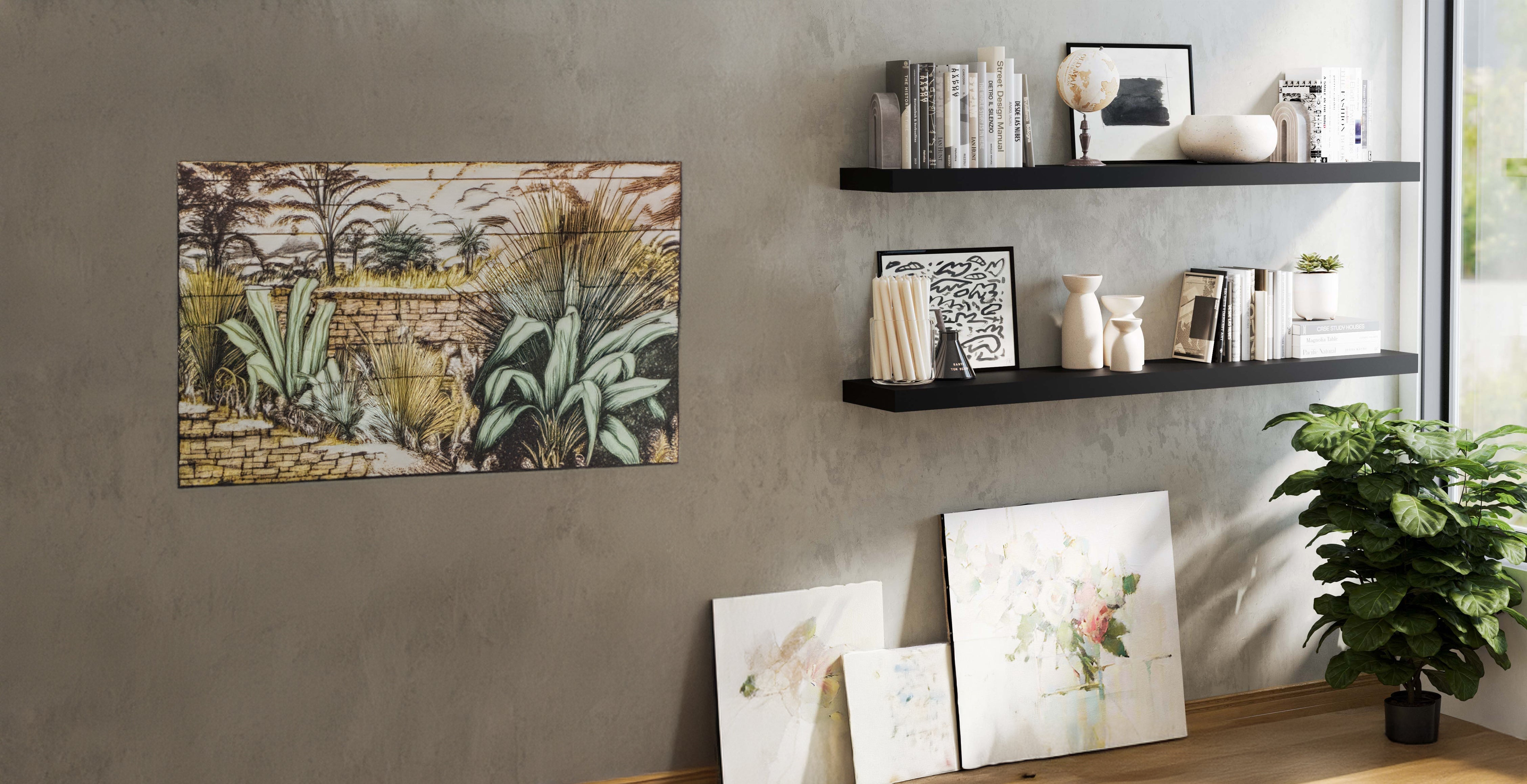 A modern interior featuring two sleek black floating shelves mounted on a textured gray wall. The shelves hold books, decorative objects, and framed artwork. Below, framed pictures lean against the wall, and a potted plant adds greenery.