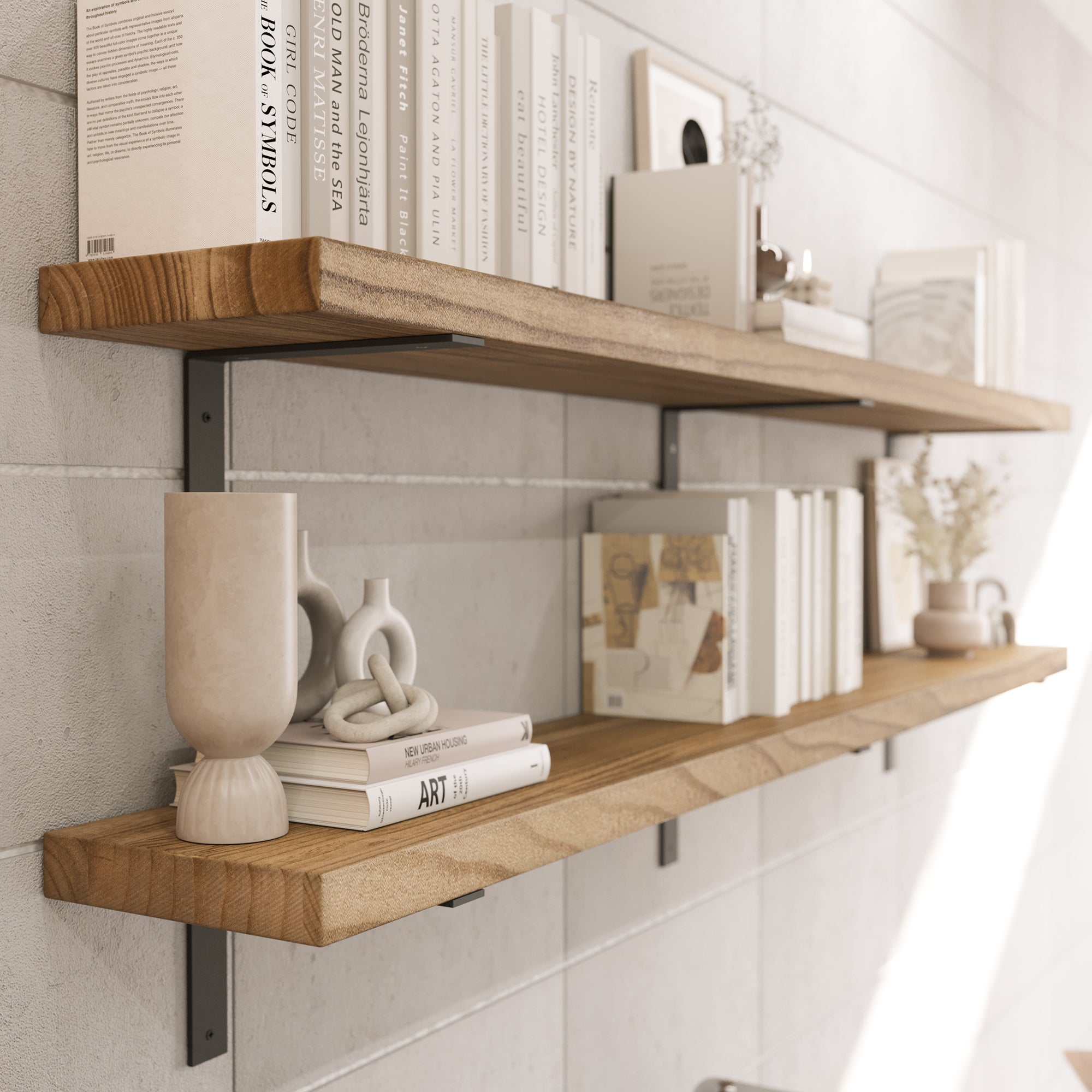 Two wooden floating shelves mounted on a white tiled wall with black metal brackets. The shelves display a minimalist arrangement of books, vases, sculptures, and framed artwork in neutral tones, creating a modern aesthetic.