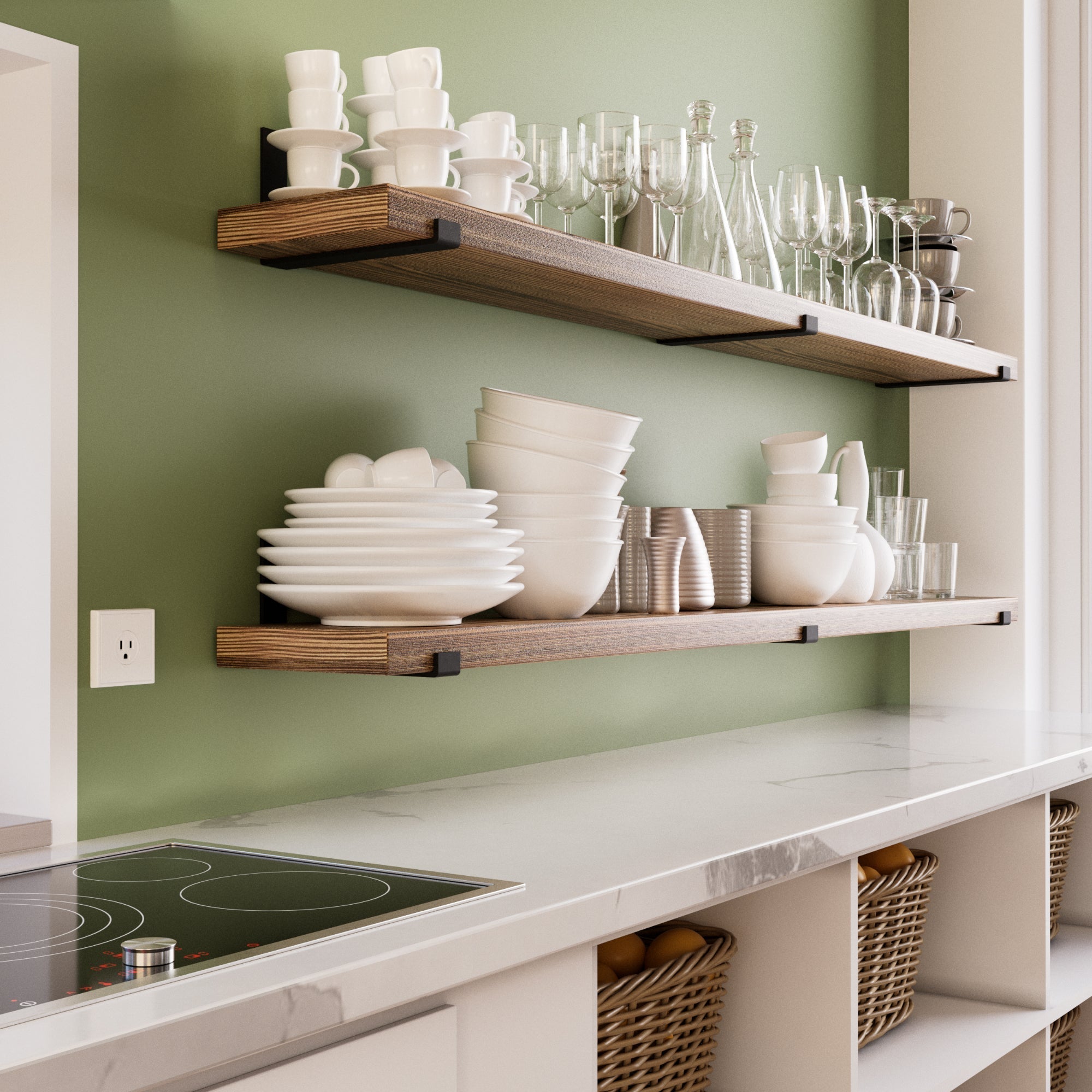 A stylish kitchen with two wooden floating shelves mounted on a sage green wall. The shelves hold neatly stacked white dishes, glasses, and cups. Below, a marble countertop with woven baskets adds warmth and organization.