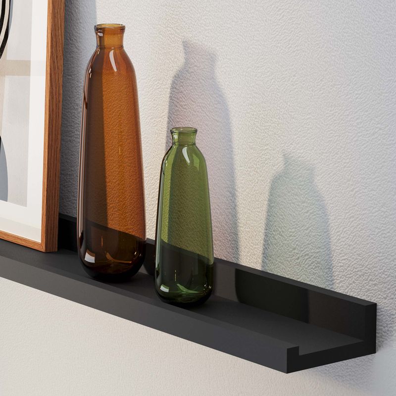 A modern decor with a tall brown bottle and a shorter green bottle on a black wall shelf, casting shadows.