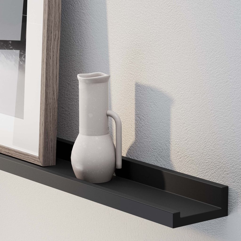 A close-up of a picture frame and ceramic jug on a 60''black floating shelf against a textured wall.