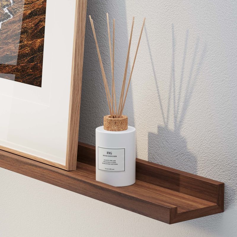 A modern diffuser with reed sticks on a 72 inch floating shelf walnut beside an abstract framed artwork, creating a serene atmosphere.