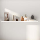 A minimalist floating white shelf, holding books and decor pieces, mounted against a plain wall. This setup highlights the shelf’s modern design, blending seamlessly into a clean and contemporary interior.