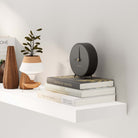 A close-up view of a white shelf with invisible brackets showcasing decor such as books and a stylish black clock, demonstrating how the shelf enhances the look of small decorative items.