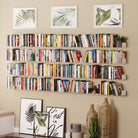 Wall-mounted white bookshelves filled with books and small plants, paired with botanical art and wicker decor, adding a stylish and organized look to the room.