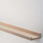 An empty natural long shelf for wall is mounted on a white textured wall, embodying simplicity and clean design, with plenty of negative space.