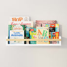 The kids book shelf used as a book display, showcasing a variety of colorful children's books. The white shelf and natural wooden rod contrast beautifully with the vibrant book covers.