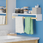 A sleek white wall shelf with a natural wooden rod, perfect for bathroom use, holding towels and various jars with toiletries. Mounted above a modern sink and against a vibrant blue wall for a fresh look.