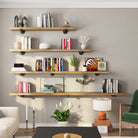 Four wooden shelves with different length options mounted with pipe brackets, styled with books, plants, and decor for a cozy living room vibe.