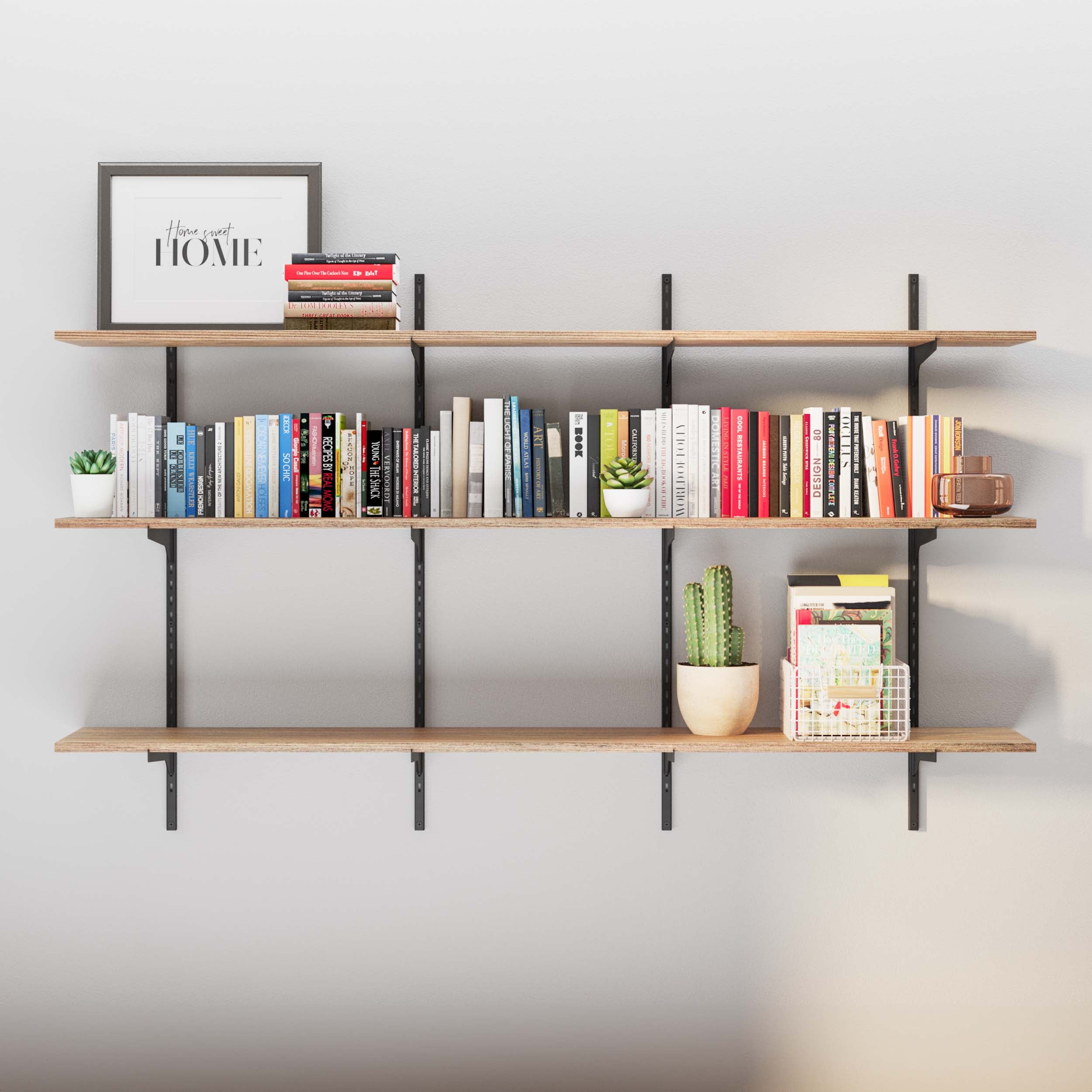 3 tier shelf burnt with ''Home sweet HOME'' writing, a cactus and stylish books on it, against a white wall.