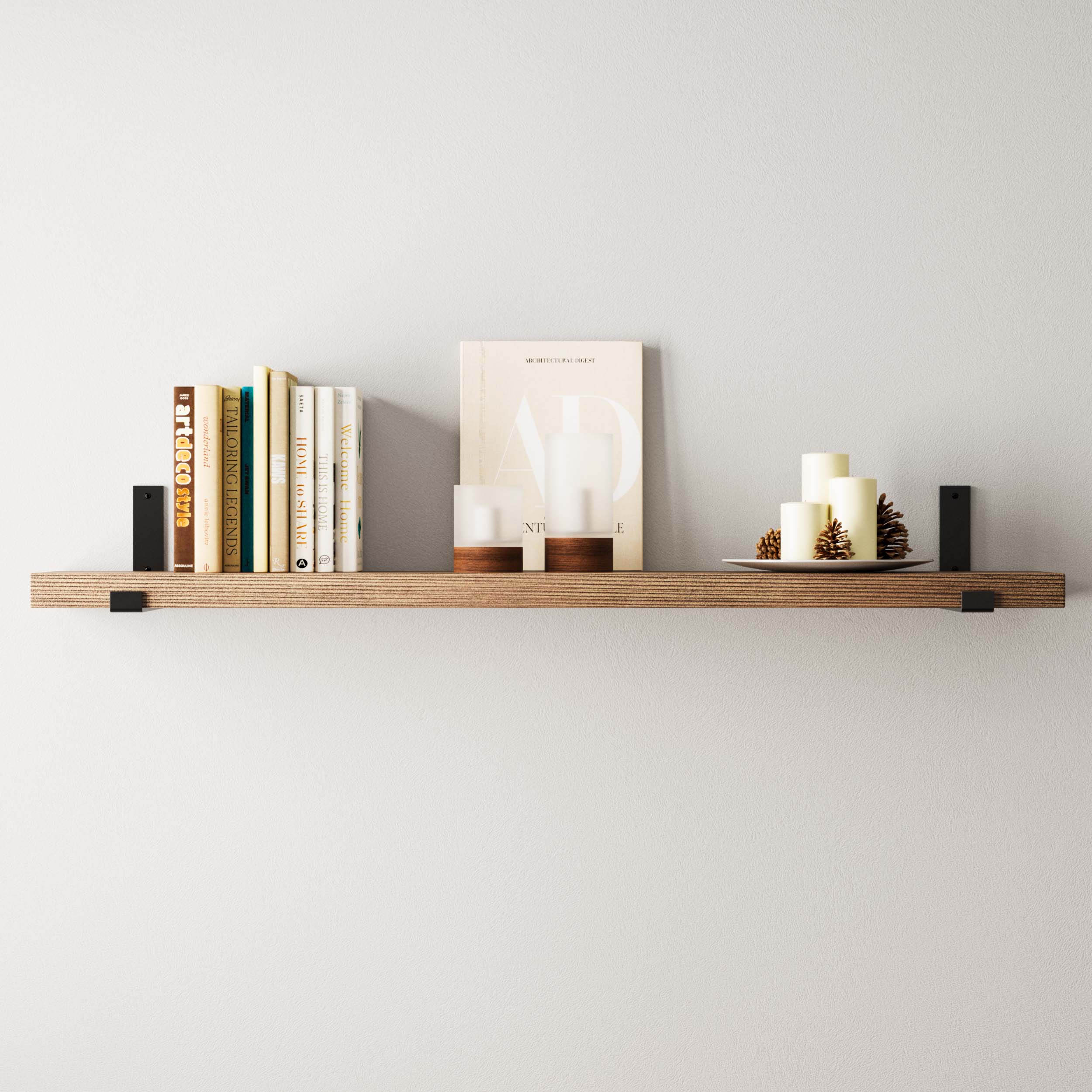 Stylish candles and books on a wall book shelf with black brackets agaisnt  a white textured wall.