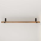 An empty rustic wooden shelf with black metal brackets against a white wall.