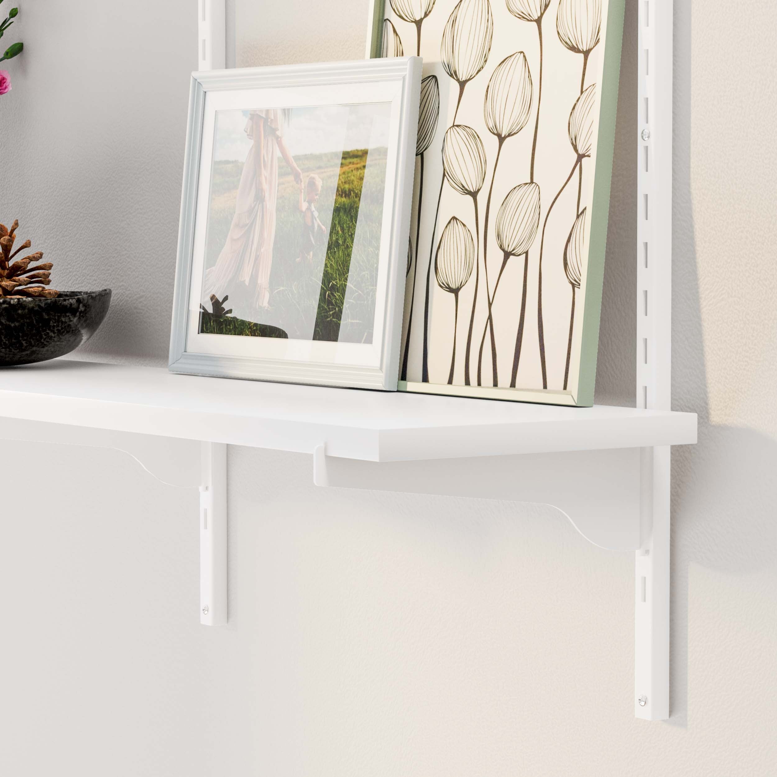 White shelf displaying an elegant photo frame beside a tall botanical print, with a warm ambiance.