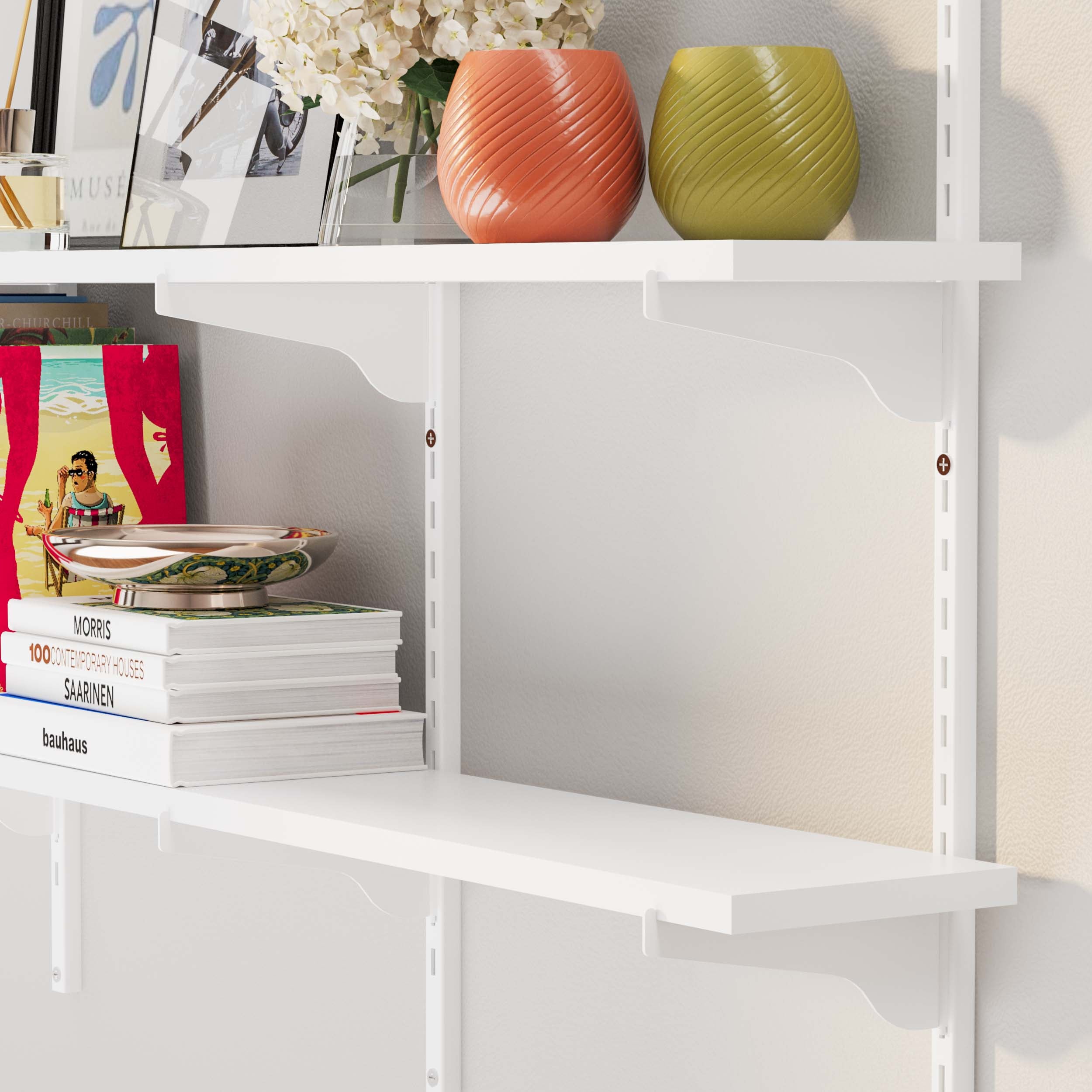 A close-up of white adjustable shelves with colorful vases, a tray, and a stack of books.