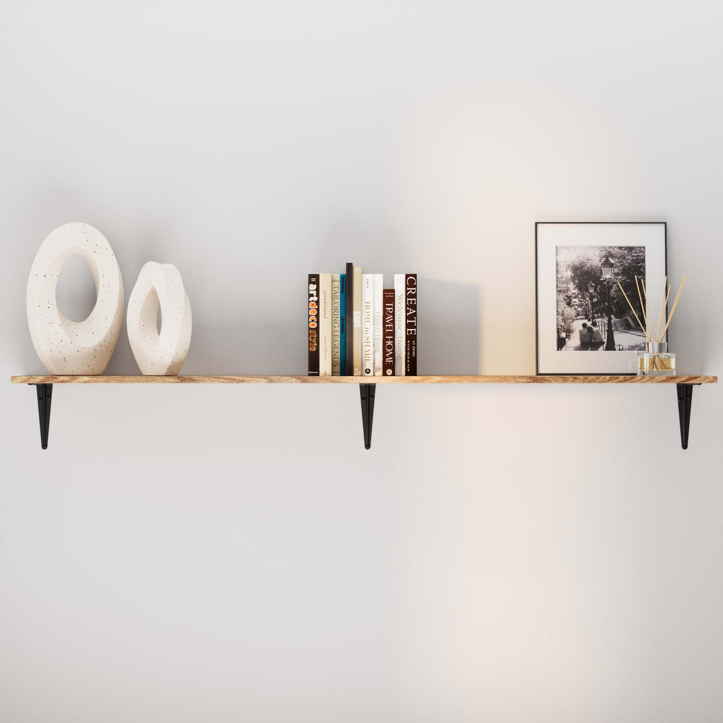 A stylish floating shelf burnt color holds two modern art sculptures, a stack of books, a framed black and white photo, and a decorative diffuser.