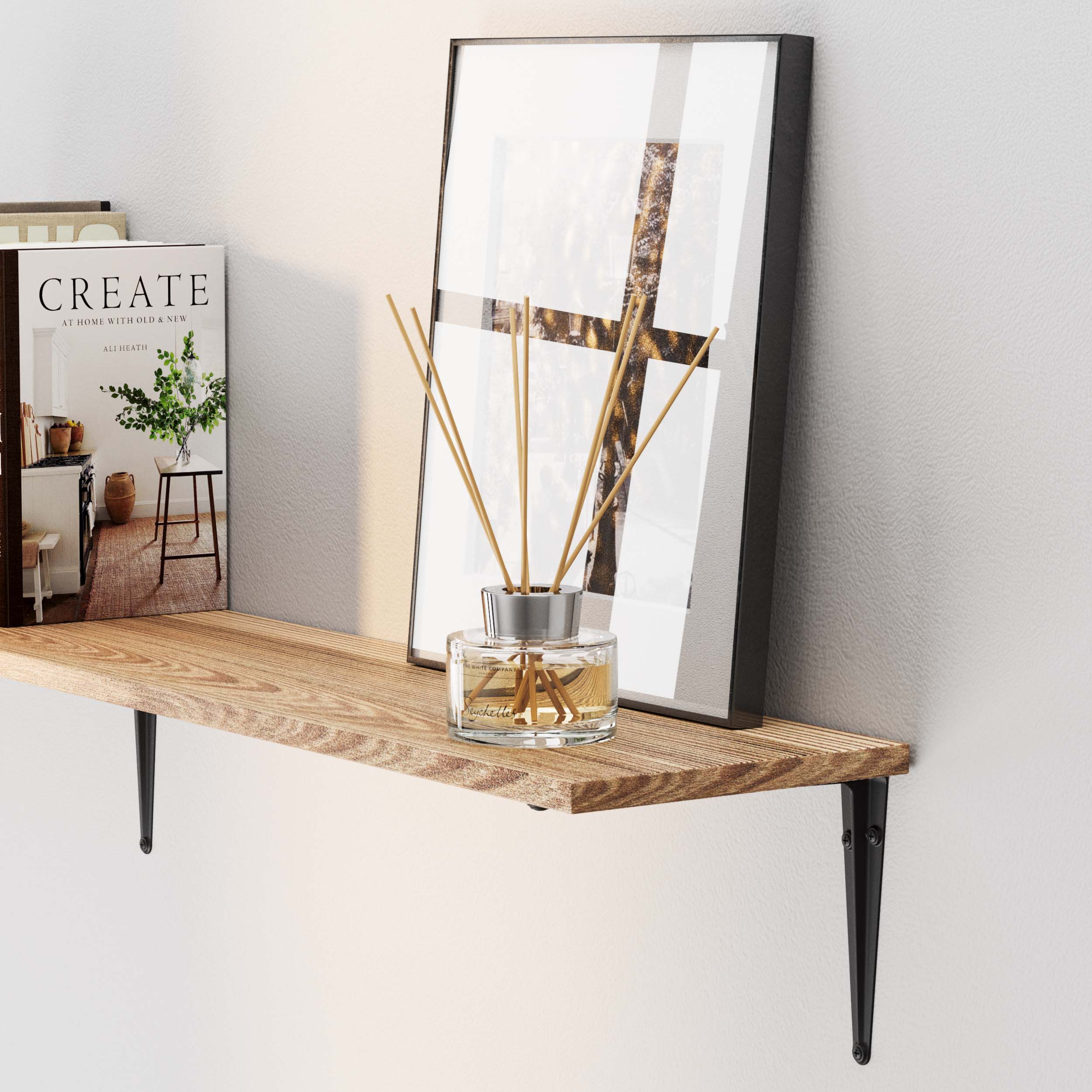 A modern wall storage shelf burnt displays a framed abstract art piece, a decorative reed diffuser, and a stylish magazine on a white wall.