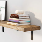 A close-up view of a floating shelf for wall burnt holding a stack of varied design books topped with a decorative vase.