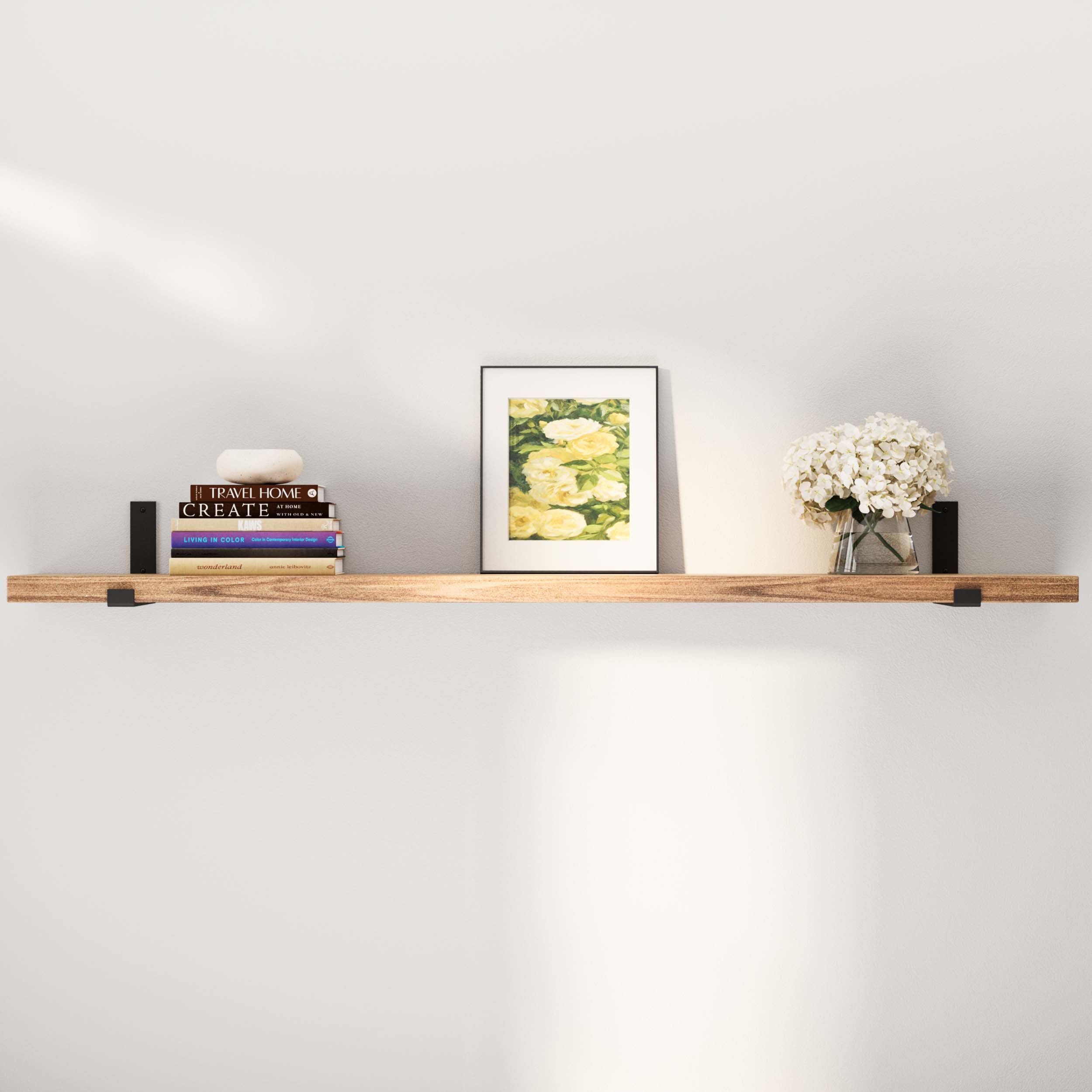 A single long wooden shelf on a wall displaying books and a vase of white flowers, creating a minimalistic aesthetic.