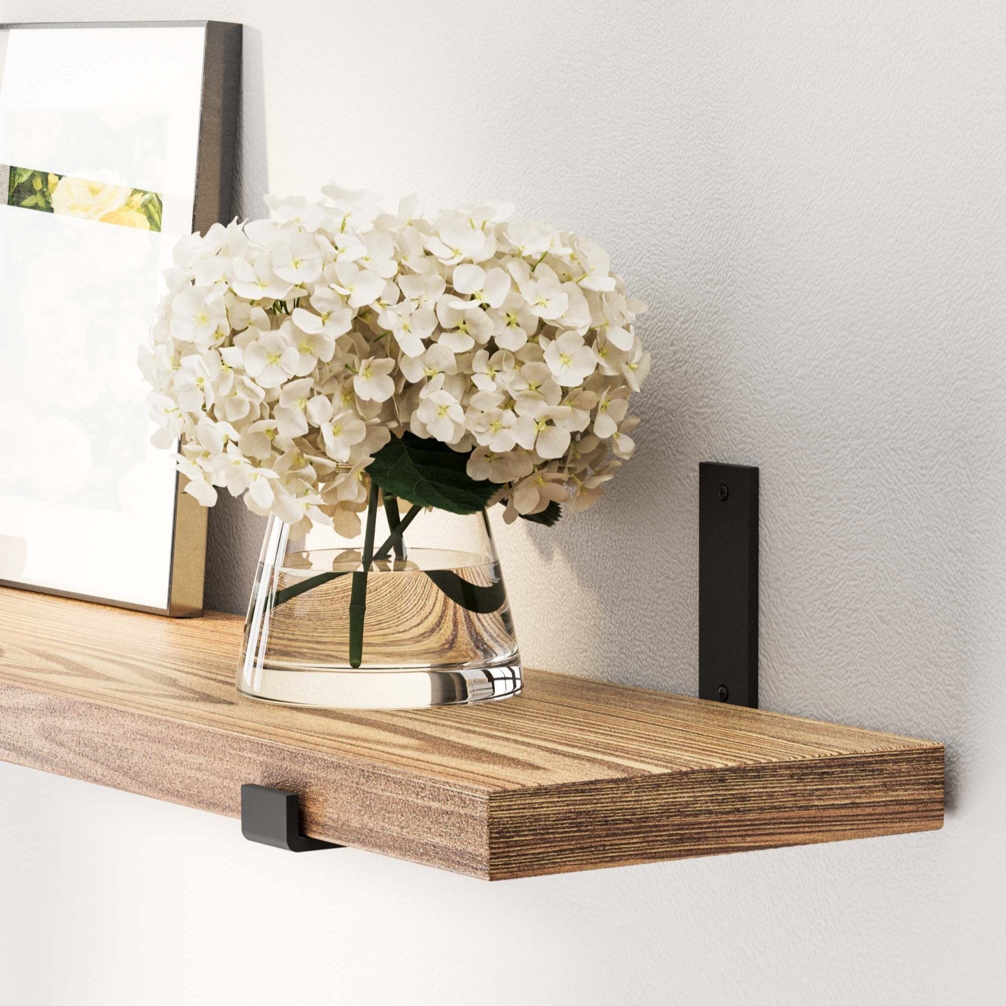 Close-up of a wood shelf burnt holding a vase with white flowers and a framed picture, showcasing elegant simplicity.