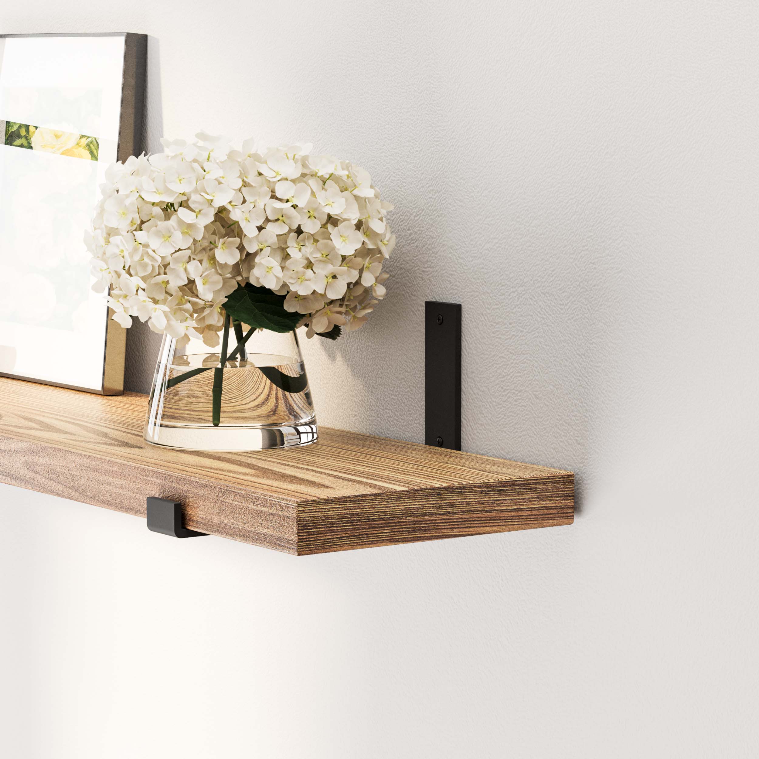 Close-up of a wood shelf burnt holding a vase with white flowers and a framed picture, showcasing elegant simplicity.