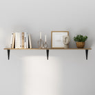 Minimalist wall shelf with black metal brackets, neatly arranged with white books, candles, a framed line art, and a small potted plant, styled against a light gray wall.