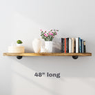 Minimalist styling with books, candles, and flowers on a 48 inch rustic wall shelf with pipe brackets.