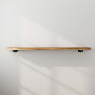 A minimalist floating shelf mounted on a white wall, showcasing its natural wood finish and sturdy pipe bracket support.