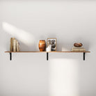 Simple, minimalistic living room wall shelf featuring a wood plank supported by black metal brackets. Decorated with books, a vase, and a picture frame for an elegant, uncluttered look.