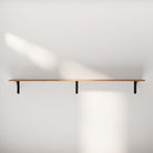 Clean and unadorned long shelf, emphasizing its floating design and natural wood grain. The focus is on the simplicity of the shelf against a plain background.