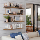 Multiple rustic shelves in burnt finish stacked against a shiplap wall, styled with books, vases, and framed art, creating a cozy and artistic vibe in a living room.