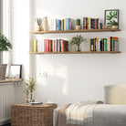 Two stacked long hanging shelves adorned with books, potted plants, and decorative pieces, creating a cozy and organized reading nook in a natural light-filled bedroom.