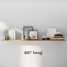 A minimalistic 60 inch long floating shelf styled with a blend of books, artistic frames, and candles, ideal for living rooms or offices. Its design focuses on simplicity and functionality.