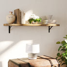 A cozy wall bookshelf featuring books, a potted plant, and a vase, mounted with black metal brackets. Styled for a charming bedside or entryway display.