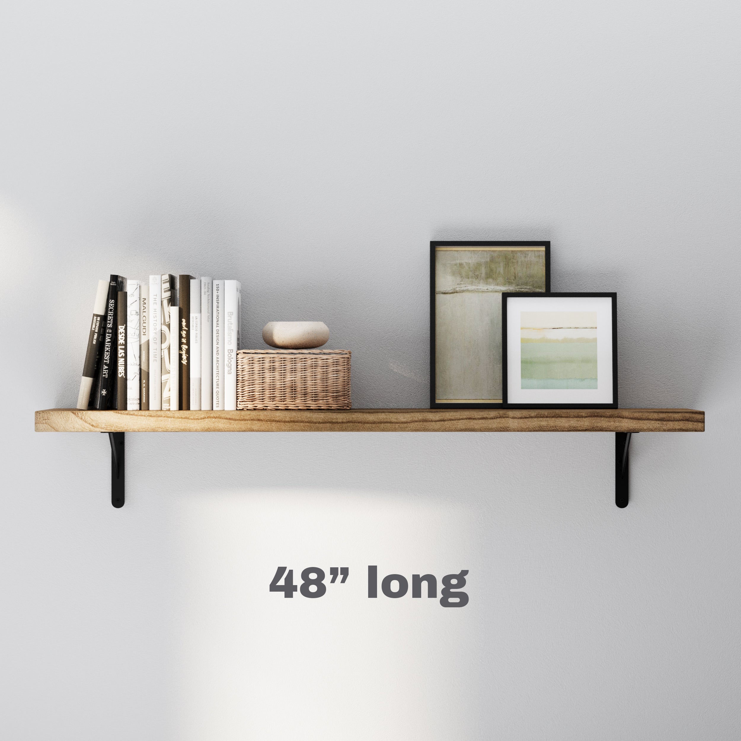 A single 48 inch long floating shelf with black metal brackets, showcasing books, a wicker basket, and framed art. Ideal for small spaces needing functional yet aesthetic storage.