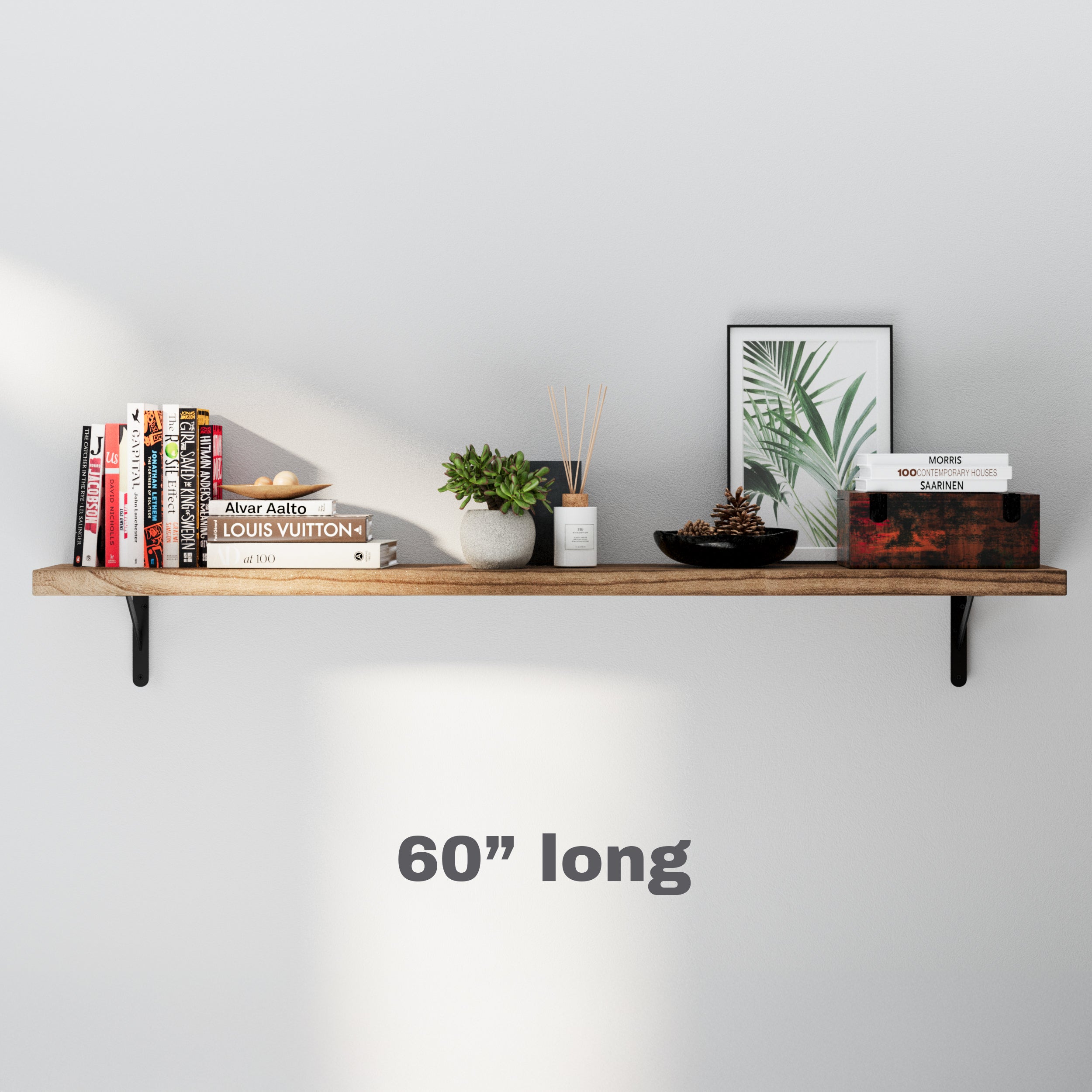 A 60 inch long wall bookshelf styled with books, a framed plant print, a candle, and a decorative bowl. The minimalist arrangement highlights functionality and elegance.