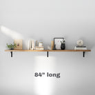 A sleek 84 inch long floating shelf with a warm wood finish, adorned with decor items like books, vases, and a clock, showcasing a minimalist and functional design.