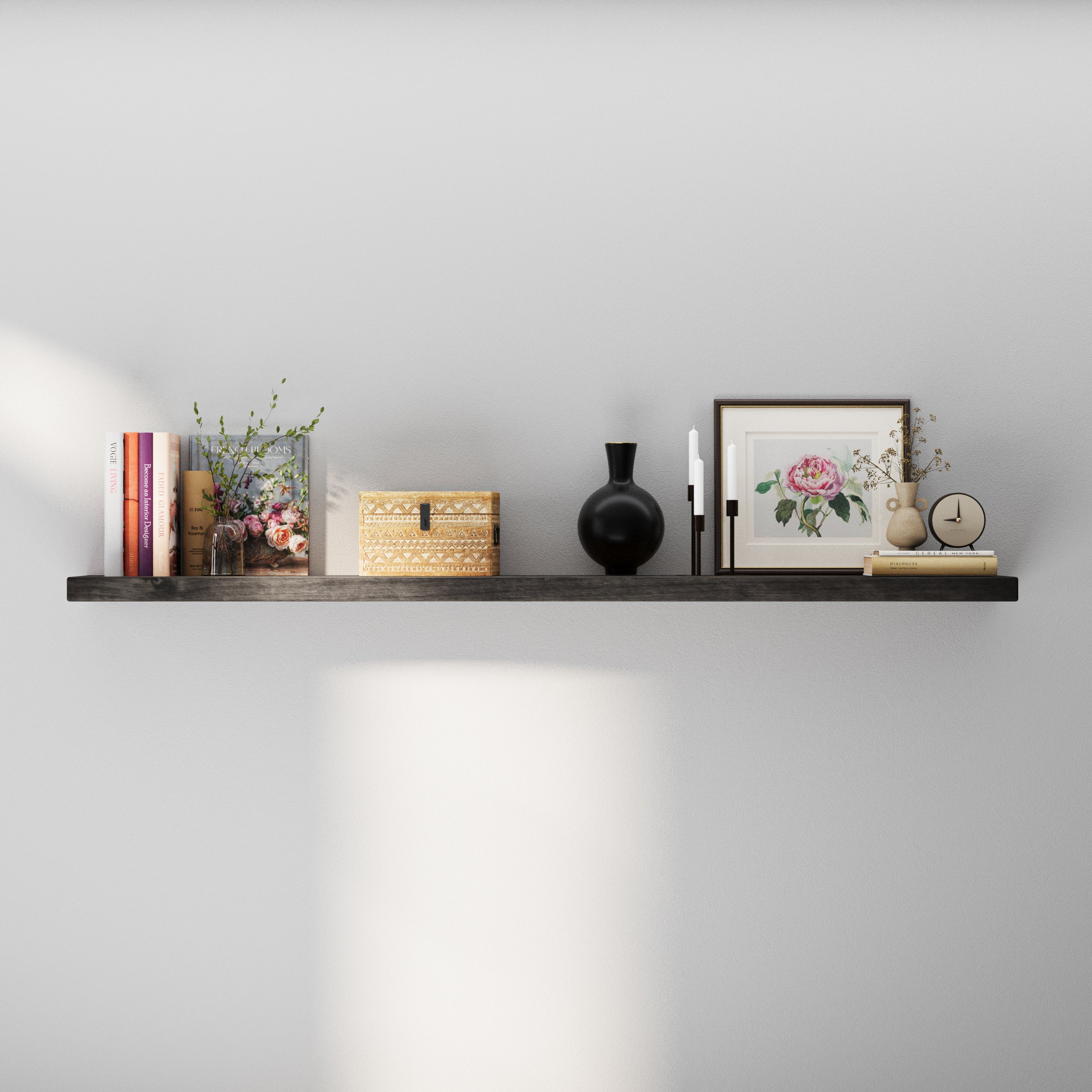 A minimalist floating shelf with a dark wood finish is styled with books, decorative vases, candles, a floral frame, and a small clock—creating a warm, elegant display against a light gray wall.