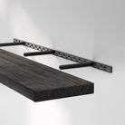 Dark-stained wooden shelf being mounted with a hidden bracket system, highlighting the sturdy steel structure for a secure, invisible wall-mount design.