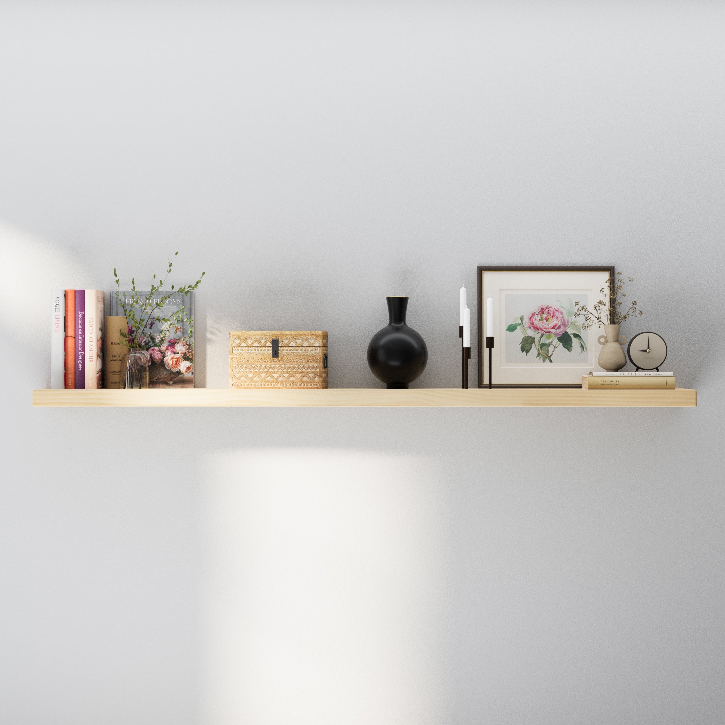 A 60" floating shelf with hidden bracket in natural wood finish styled with books, a black vase, framed artwork, candles, and a decorative clock—blending simplicity with elegance on a neutral wall.