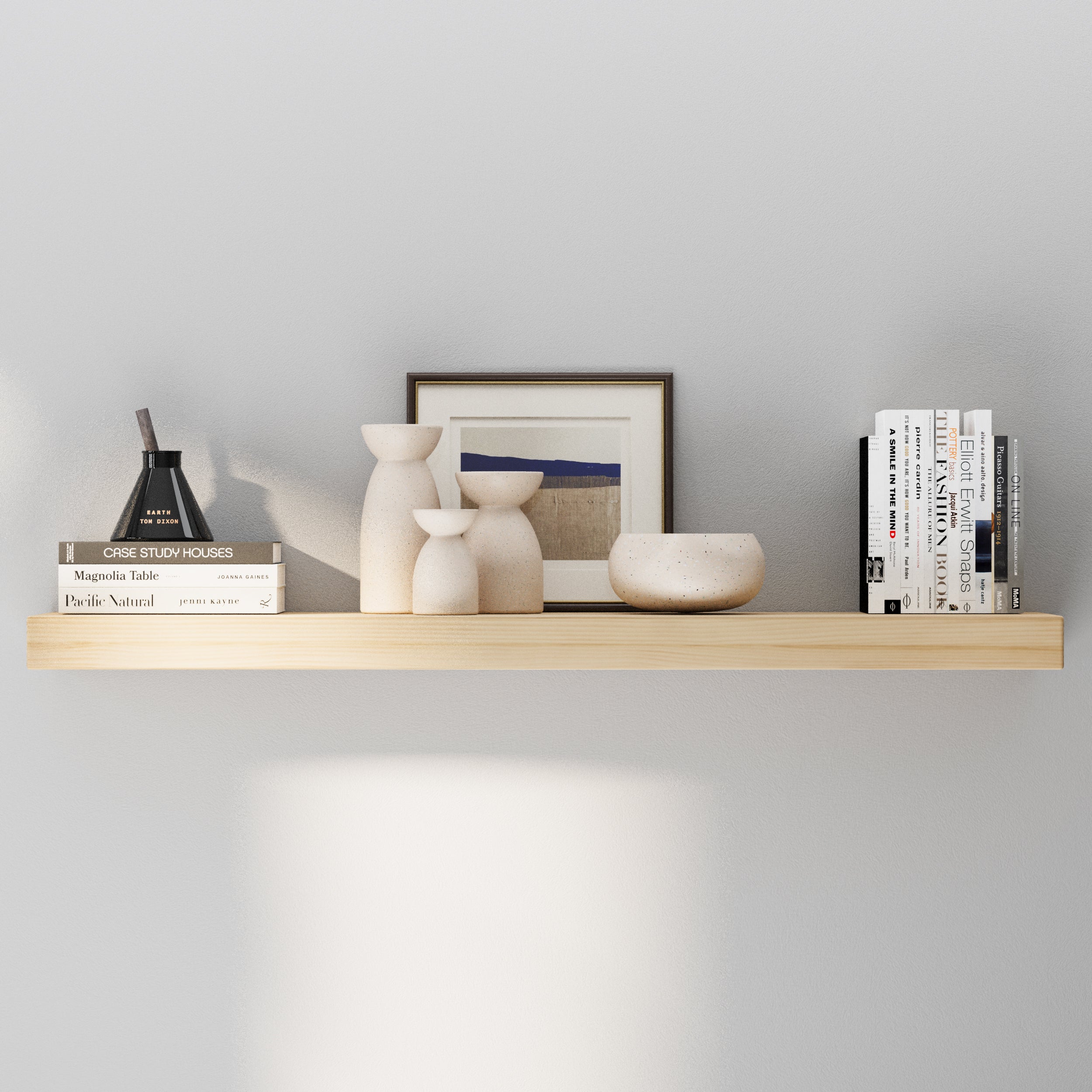 A single floating shelf in a natural wood finish styled with ceramic vases, neutral-toned books, and framed wall art, offering a minimalist and airy decorative look.