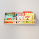 A natural wood wall shelf filled with children's books, mounted on a light gray wall. The shelf holds colorful book covers, making it an inviting and organized space for young readers.