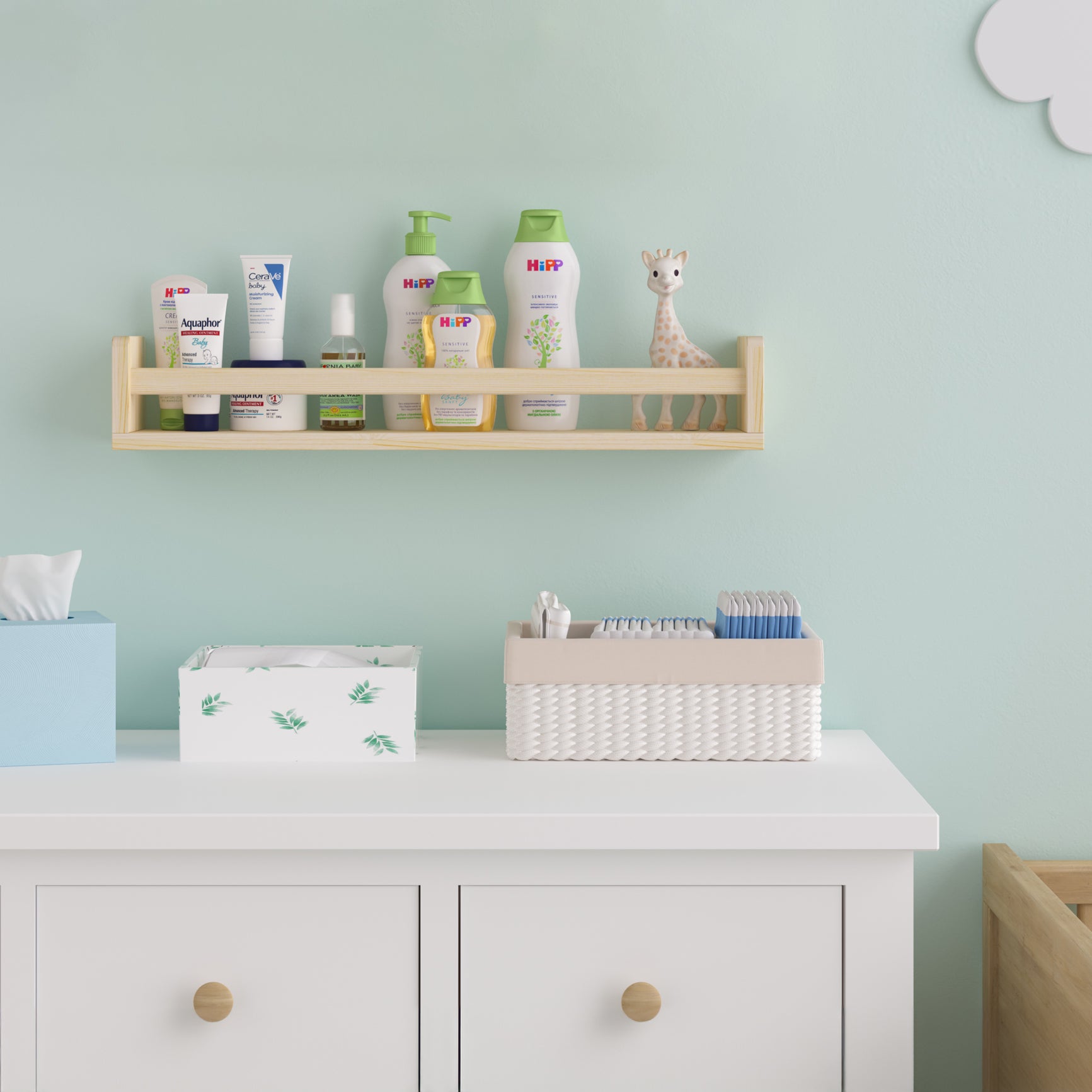 A natural wood kids shelf in a nursery, holding baby care products and a small giraffe toy. Mounted on a mint green wall above a white dresser, creating an organized and serene space for baby essentials.
