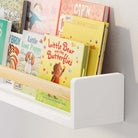 Close-up of the white book shelf kids with a natural wood rod holding children's books, showcasing its sturdy construction and smooth finish. The detailed view highlights the craftsmanship and practical design.