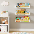 Three white kids shelves with natural wood rods in a children's room, filled with books and toys. Mounted on a light gray wall beside a white storage unit, creating a playful and organized space.