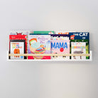A white wall kids shelf with a natural wood rod filled with children's books, mounted on a light gray wall. The shelf holds colorful book covers, creating an inviting and organized space for young readers.