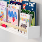 Close-up of the white wall shelf for kids room with a natural wood rod holding children's books, showcasing its sturdy construction and smooth finish. The detailed view highlights the craftsmanship and practical design.