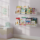 Two white wall mount kids shelves with natural wood rods filled with children's books and a toy, mounted on a soft pink wall. Positioned above a decorative storage box, creating an organized and playful space for children.