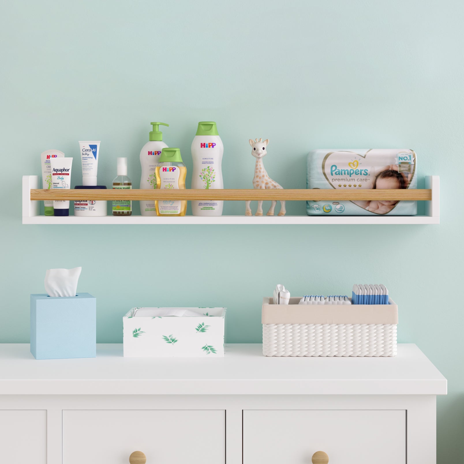 A white wall storage shelf for kids room with a natural wood rod in a nursery, holding baby care products and a giraffe toy. Mounted on a mint green wall above a white dresser, providing an organized and charming setup for baby essentials.